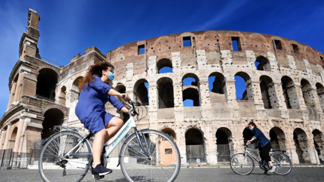 Women ride a bicycle past the Colosseum monument in Rome on May 8, 2020, during the country's lockdown aimed at curbing the spread of the COVID-19 infection, caused by the novel coronavirus. - The number of deaths from coronavirus in Italy now exceeds 30,000, officials said on May 8, 2020. The country's Civil Protection Agency said that 30,201 people had died of the virus, 243 more than on May 7. Italy is the second European country, after Britain to see more than 30,000 COVID-19 deaths. (Photo by Alberto PIZZOLI / AFP)
